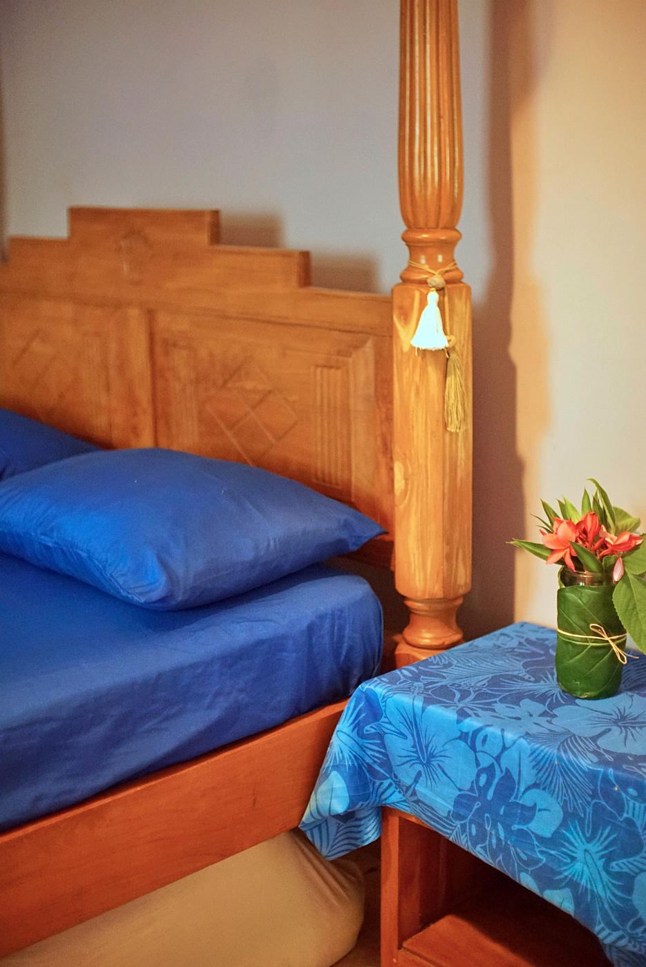 A guest room at Fare Om with a carved wooden bed and fresh flowers